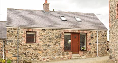 Image shows front of stone cottage with wooden door and gravel driveway.