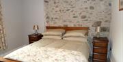 Images shows double bed against feature wall of exposed stonework.