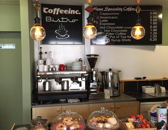 Image shows front counter of Coffee Inc premises with barista machines and traybakes and scones in covered display.