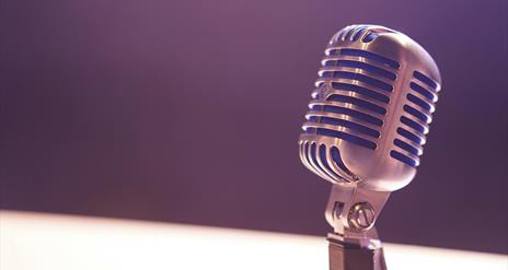 Picture of a silver coloured microphone with a purple background